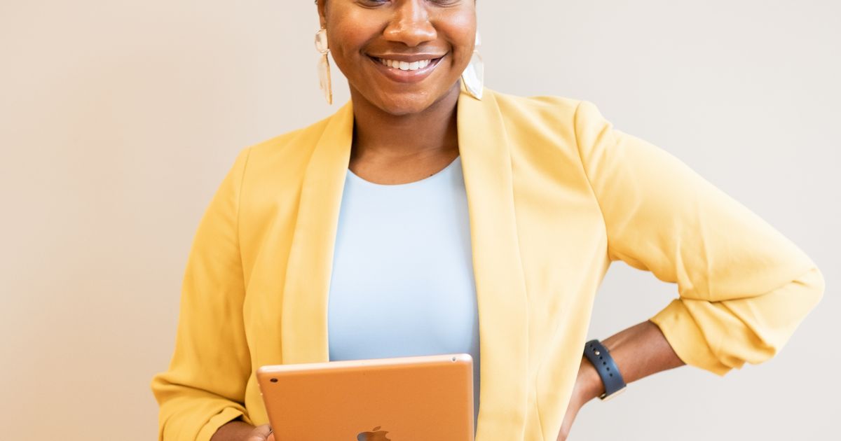 A smiling businesswoman in a yellow blazer holding a tablet