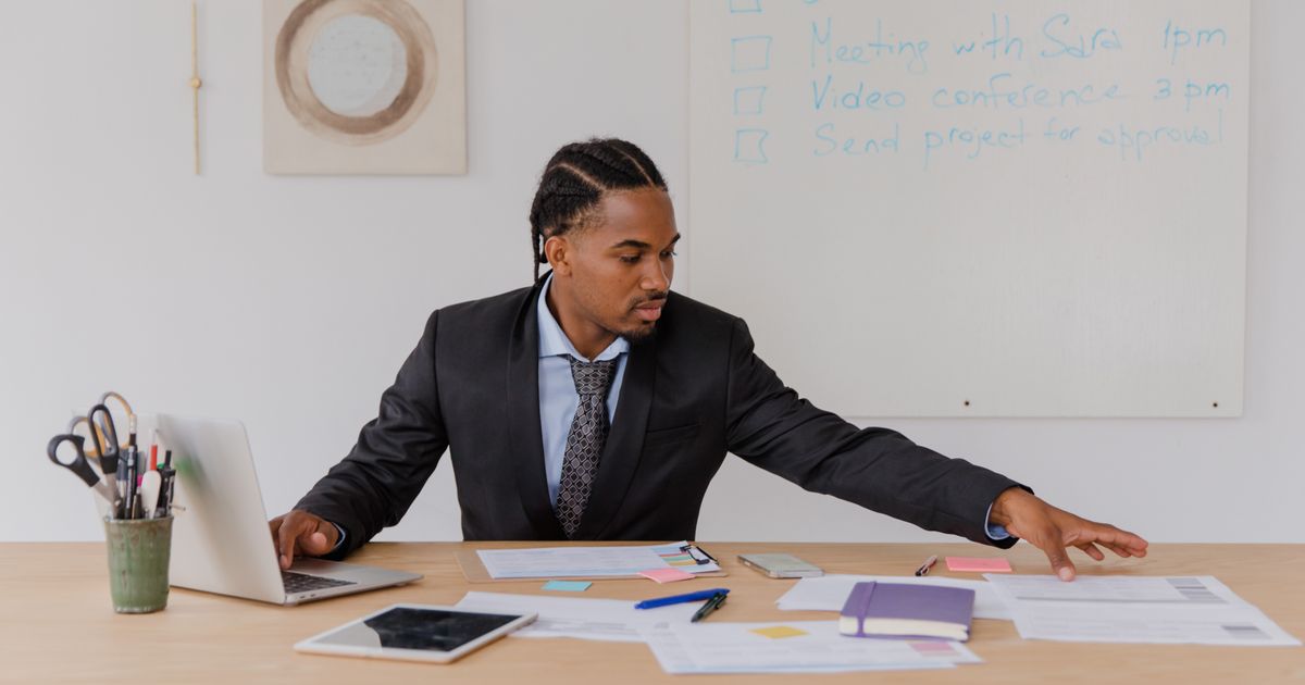 A man in a suit sitting at his desk reaching for documents