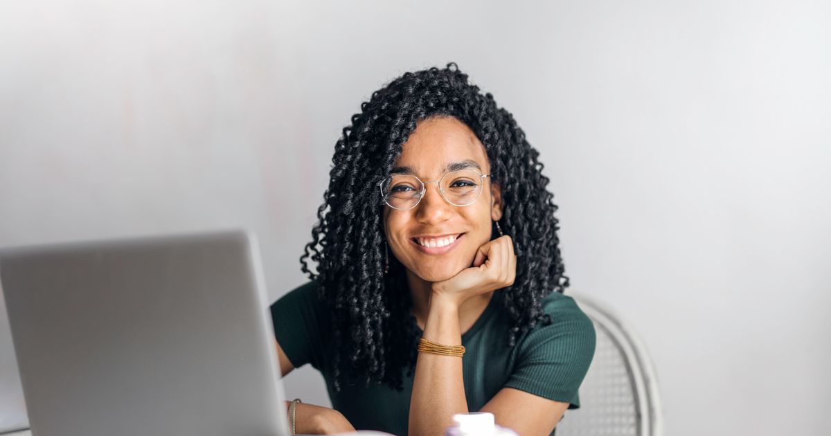 A smiling woman with curly hair sitting at a laptop