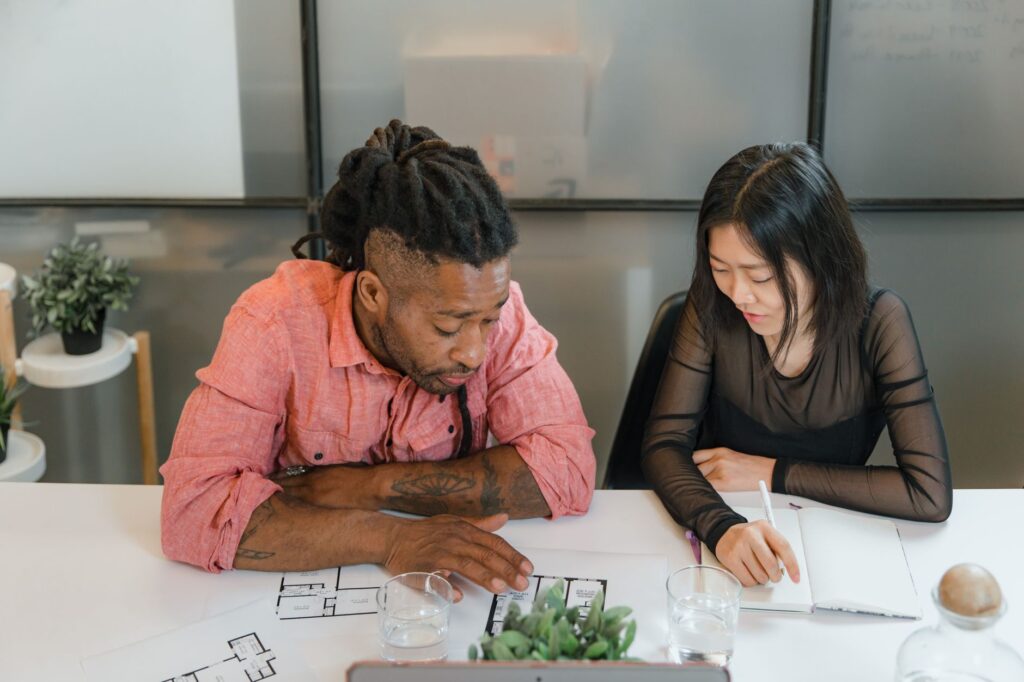 man and woman sitting at table with blueprints at office