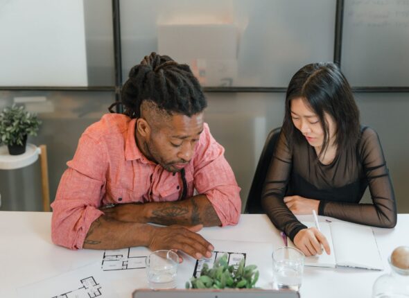 man and woman sitting at table with blueprints at office